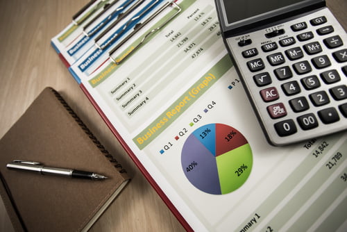 Printed business reports - showing graphs and figures - alongside a calculator, notebook and pen